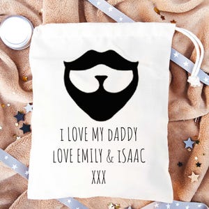 May include: White cotton drawstring bag with a black and white illustration of a beard and the text "I love my daddy love Emily & Isaac XXX".