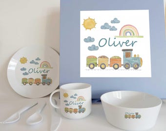 May include: A white dinnerware set including a plate, a mug, a bowl, and three white utensils. Each piece features a watercolor illustration of a train, a rainbow, clouds, a sun, and the name Oliver printed in blue script text on a light blue box.