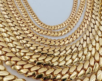 May include: A collection of gold-colored Cuban link chain necklaces in various sizes. The necklaces are arranged in a layered display, showcasing the different widths and lengths of the jewelry. The chains have a polished, reflective surface.