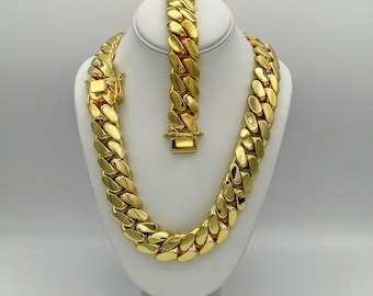 May include: A gold chain necklace and bracelet set. The chain is thick and has a curb link design. The set is displayed on a white mannequin.