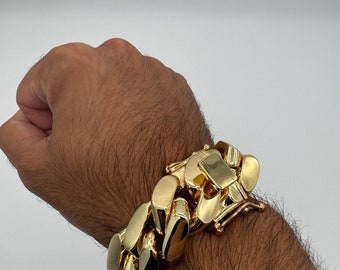 May include: A gold chain bracelet with a large, chunky link design. The bracelet is worn on a person's wrist.