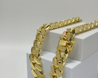 Può includere: Una collana a catena d'oro con uno stile a maglia cubana. La catena è spessa e ha una finitura lucida. La catena è esposta su una piattaforma bianca.