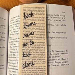May include: A close-up of a vintage book bookmark with a hand-drawn illustration of a book and the words "book lovers" and "never go to bed alone". The bookmark is made of paper with a brown and white background.
