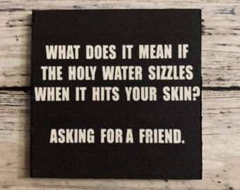 May include: Black square sign with white text that reads "WHAT DOES IT MEAN IF THE HOLY WATER SIZZLES WHEN IT HITS YOUR SKIN? ASKING FOR A FRIEND."