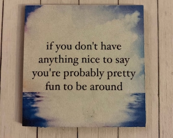 May include: A light brown square sign with a blue watercolor sky and water background. The sign has the text "if you don't have anything nice to say you're probably pretty fun to be around".