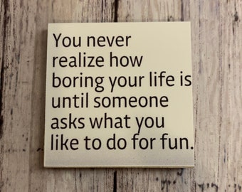 May include: A yellow sign with black text that reads "You never realize how boring your life is until someone asks what you like to do for fun."