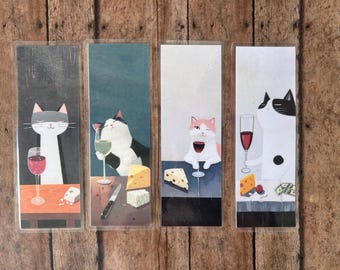May include: Set of four bookmarks featuring illustrations of cats drinking wine and cheese. Each bookmark is printed on white cardstock and has a clear plastic coating.