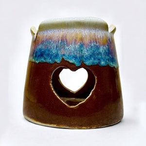 May include: A brown ceramic oil burner with a heart-shaped opening. The burner has a blue and purple glaze with a white rim.