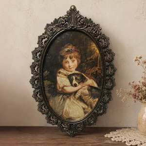 May include: An oval wall portrait featuring a painting of a child holding a black and white dog. The artwork is encased in an ornate, dark metallic frame with intricate scrollwork and decorative detailing along the entire outer edge.