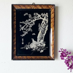 May include: Vintage framed artwork featuring a black background with a detailed white illustration of a bird, tree, and foliage. The frame is a dark wood with a patterned design. The artwork has Japanese characters in the lower left corner.