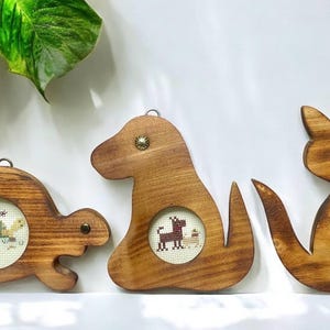 May include: Three wooden animal-shaped picture frames with embroidered images of a turtle, a dog, and a cat. The frames are brown and have a rustic look.