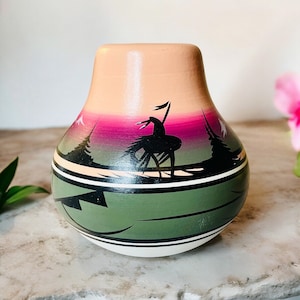 Peut inclure: Un petit vase en céramique peint à la main avec un motif vert, rose et blanc. Le vase représente une silhouette d'un Amérindien à cheval.