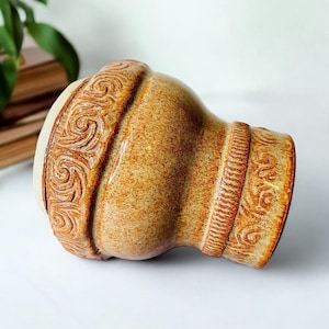 May include: A ceramic vase with a brown and white glaze. The vase has a textured surface with a decorative pattern around the top and bottom.