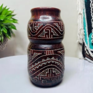 May include: A dark brown ceramic vase with intricate carved designs. The vase has a rounded body and a slightly flared top.