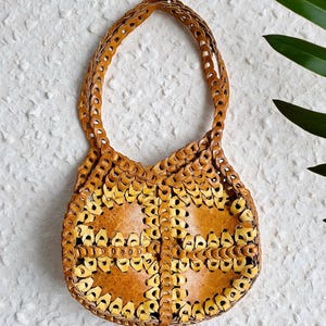 Peut inclure: Un sac à main en cuir marron clair fait à la main, avec un motif tissé unique. Le sac a une forme arrondie, une poignée robuste et des motifs découpés complexes. La couleur est un mélange de marron clair et foncé, créant un aspect texturé.