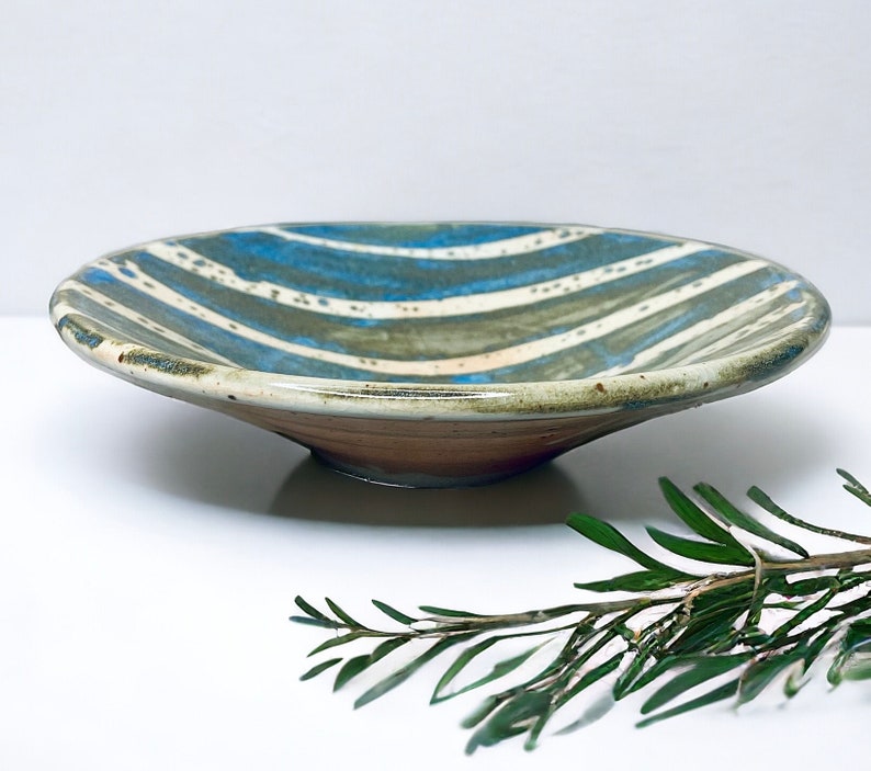 K&ouml;nnte beinhalten: Eine Keramik-Servierplatte mit einem blau-wei&szlig; gestreiften Design. Die Platte hat einen leicht erh&ouml;hten Rand und einen braunen Boden.
