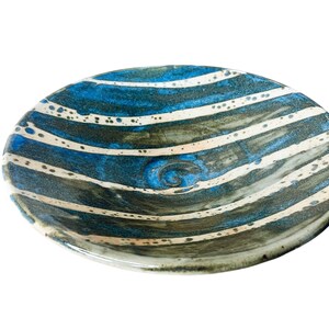 K&ouml;nnte beinhalten: Eine Keramiksch&uuml;ssel mit einem gestreiften Muster in Blau, Wei&szlig; und Braun. Die Sch&uuml;ssel hat eine leicht abgerundete Form und eine gl&auml;nzende Oberfl&auml;che.