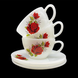 May include: Three white ceramic teacups with red rose floral designs stacked on top of each other. The cups are on a white saucer.