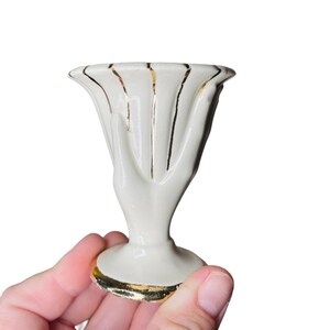 K&ouml;nnte beinhalten: Kleine, cremefarbene Keramikvase mit ausgestelltem Oberteil und Sockel. Die Vase hat vertikale Goldstreifen und Goldbesatz um den Boden und den Rand. Das Design ist elegant und vintage.