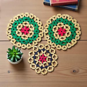 May include: Three decorative coasters made of light-colored wood, green, red, and navy blue accents. The coasters have a floral design, with a small succulent plant in a white pot to the left. Books are in the background.