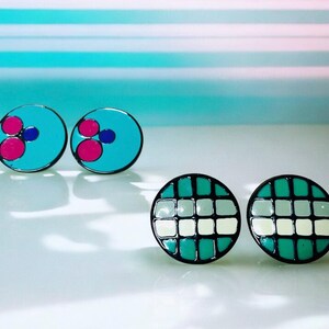 Könnte beinhalten: Ein Set mit vier bunten Ohrringen. Zwei Ohrringe sind türkisblau mit rosa und blauen Kreisen. Die anderen beiden Ohrringe sind grün mit weißen Quadraten.