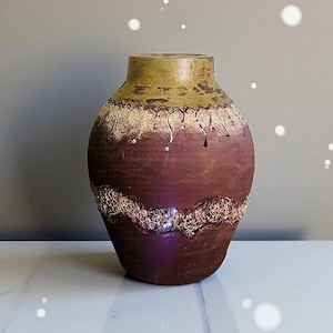 May include: A decorative ceramic vase with a textured surface. The vase features a color scheme of brown, gold, and green. The upper portion is green, transitioning to brown with gold accents and a textured band around the middle.