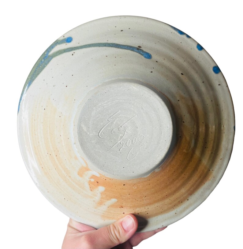 K&ouml;nnte beinhalten: Eine wei&szlig;e Keramiksch&uuml;ssel mit blauem und gr&uuml;nem Glase. Die Sch&uuml;ssel hat einen braunen Rand und eine Signatur auf der Unterseite, die "C.B. 2003" lautet.