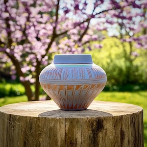 May include: A light blue ceramic vase with a wide, rounded body and a narrow neck. The surface features intricate, etched patterns in a warm copper-brown tone, including repeating leaf-like motifs and horizontal bands encircling the vessel.