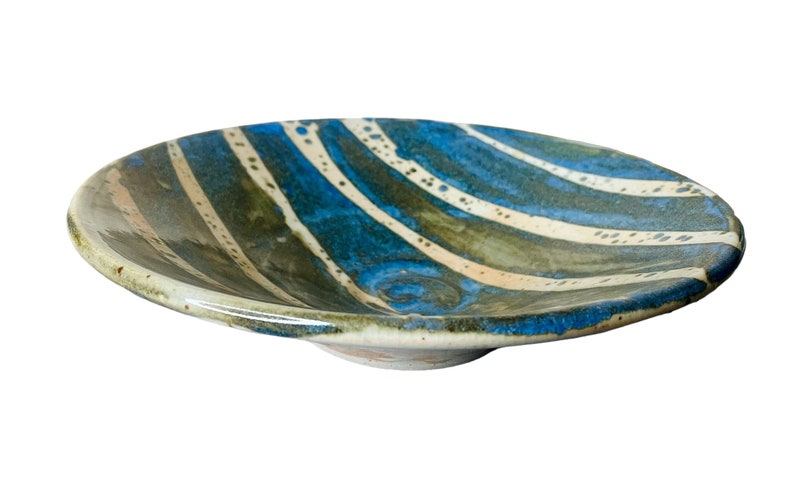 K&ouml;nnte beinhalten: Eine Keramik-Servierplatte mit einem wellenf&ouml;rmigen, blau-gr&uuml;n-wei&szlig; gestreiften Design. Die Platte ist leicht gew&ouml;lbt und hat eine gl&auml;nzende Oberfl&auml;che.