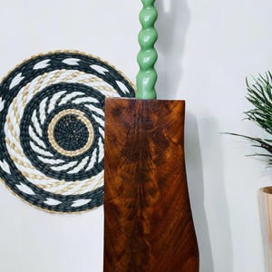 May include: A green candle with a unique spiral design sits on a dark brown wooden candle holder. The holder has a natural, rustic look and is made from a single piece of wood.
