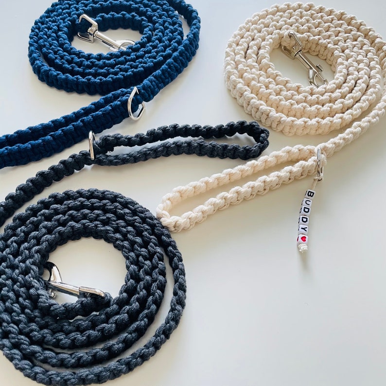 Puede incluir: Tres correas de perro de algod&oacute;n en azul marino, gris y crema. La correa crema tiene un charm que dice "BUDDY" con un coraz&oacute;n rojo.
