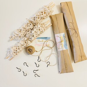 May include: A set of three macrame wall hangings wrapped in brown paper with twine, along with a ball of twine, eight black hooks, and a thank you card.