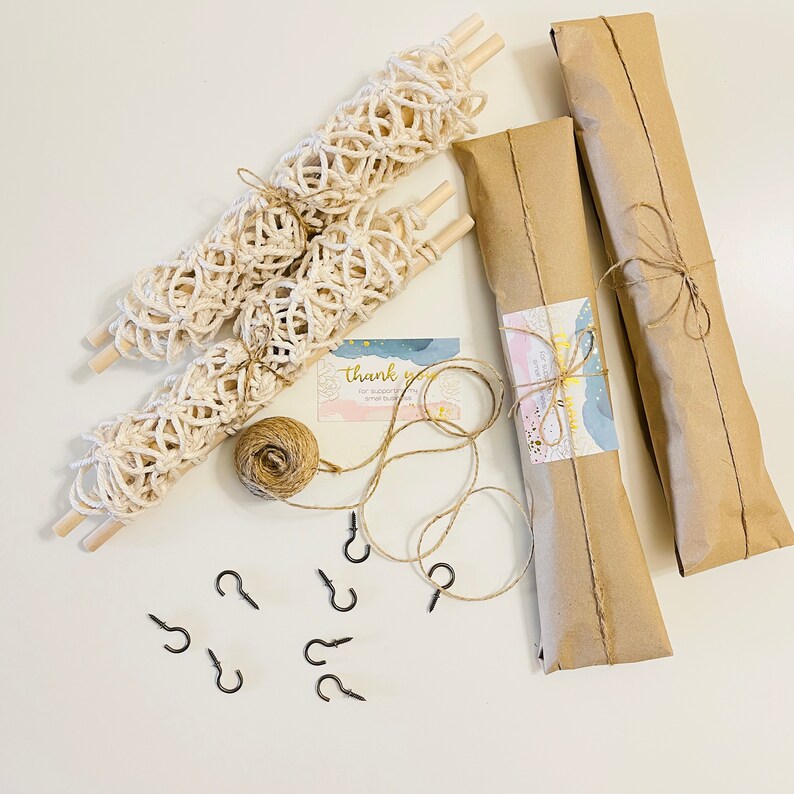 May include: A set of three macrame wall hangings wrapped in brown paper with twine, along with a ball of twine, eight black hooks, and a thank you card.
