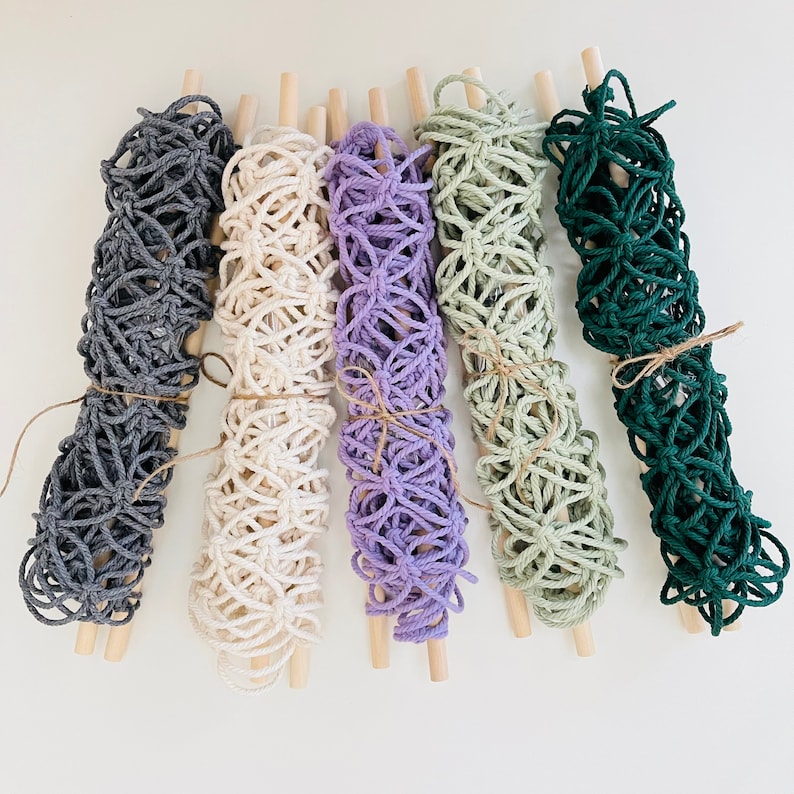 May include: Five macrame wall hangings with wooden dowels. The hangings are made with different colored cords, including gray, white, purple, green, and beige.