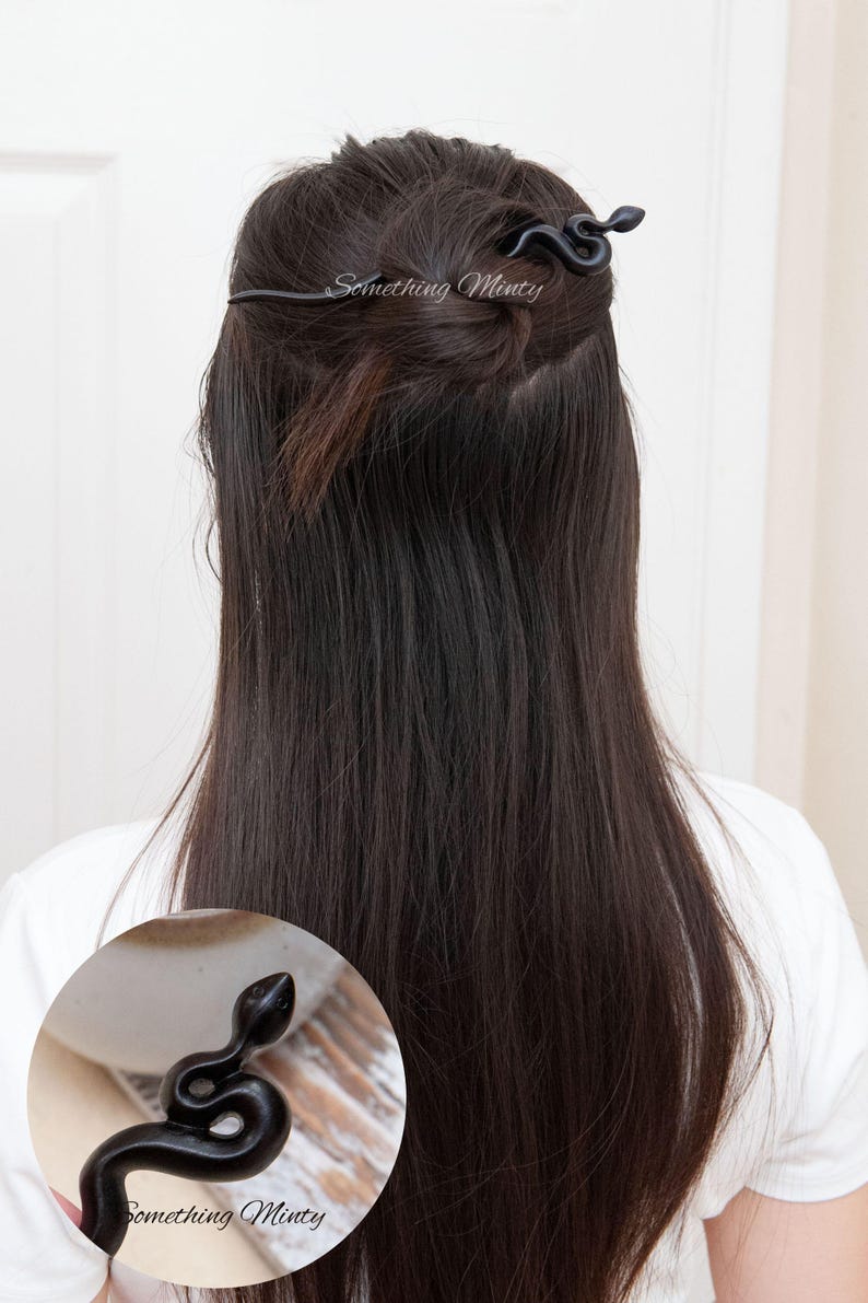 May include: Black snake hair stick with a decorative snake head. The stick is being used to hold a woman's hair in a bun.