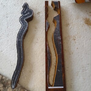 May include: Two wooden blocks with a carved design. The design is a snake on one block and a long, thin shape on the other. The blocks are both brown and have a dark stain.