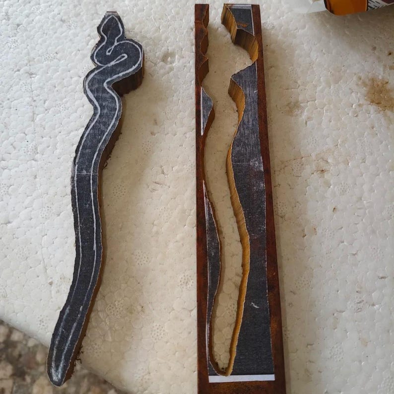 May include: Two wooden blocks with a carved design. The design is a snake on one block and a long, thin shape on the other. The blocks are both brown and have a dark stain.