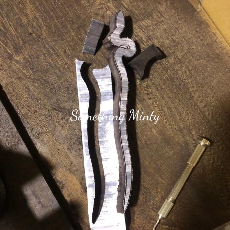 May include: A close-up of a wooden snake-shaped carving being cut out with a drill. The carving is on a white paper with the text "Something Minty" written on it.