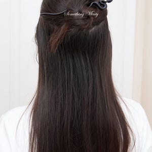 May include: Black snake hair clip with a curved design. The clip is in a woman's hair.