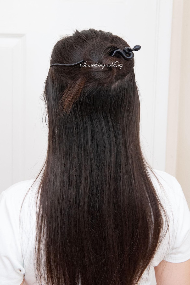 May include: Black snake hair clip with a curved design. The clip is in a woman's hair.