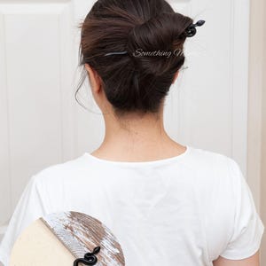 May include: Black snake hair stick with a curled tail. The stick is being used to hold a woman's hair in a bun.