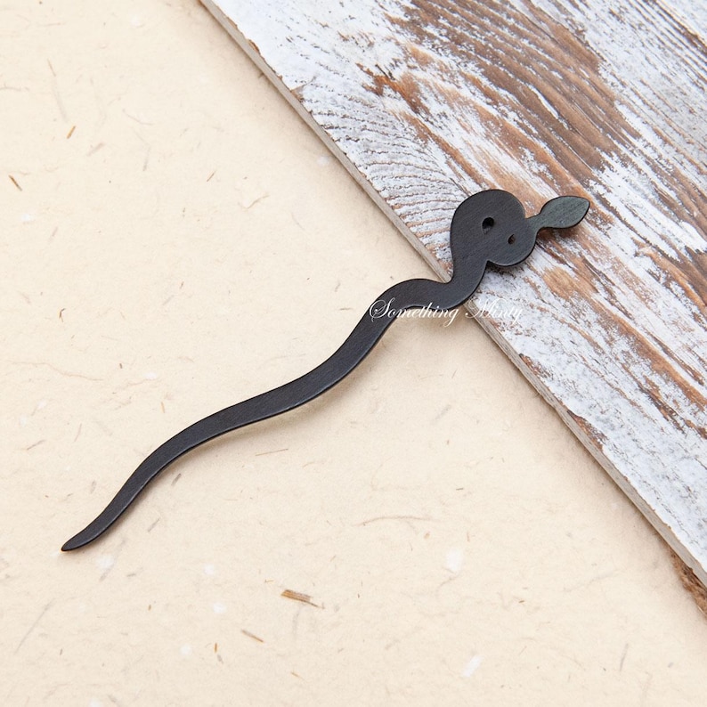 May include: Black snake-shaped hair stick. The stick is made of wood and has a smooth, polished finish.