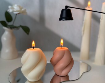 May include: Two twisted candles, one white and one pink, are lit and sitting on a silver, cloud-shaped tray. A black candle snuffer is hanging above the candles.