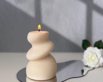 May include: A white, abstractly shaped candle with a single wick burning on a silver, irregular shaped tray.