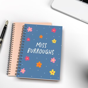 May include: A blue spiral notebook with a floral pattern and white text that says "Miss Burroughs".