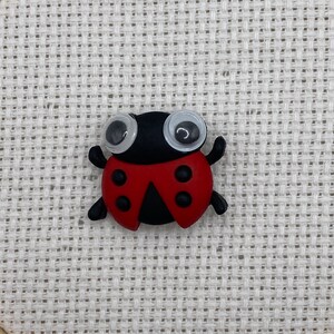 May include: A red ladybug with black spots and googly eyes. The ladybug is made of plastic and has a 3D design.
