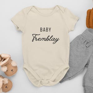 May include: A cream-coloured baby onesie with short sleeves and the text "BABY Tremblay" in black.