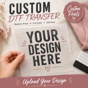 Peut inclure: Une feuille translucide carrée portant le texte noir "YOUR DESIGN HERE" avec de petites lignes décoratives et une icône de cœur. La feuille est étiquetée "CUSTOM DTF TRANSFER" avec les mentions "Ready to Press", "Full Color" et "Soft Feel".