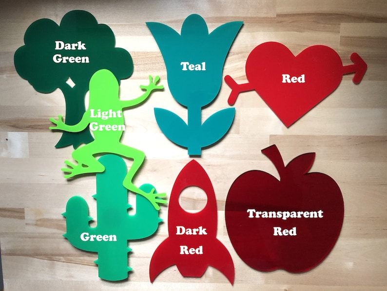 May include: Assorted laser-cut shapes in various colors, including a dark green tree, a light green frog, a green cactus, a teal flower, a red heart with an arrow, a dark red rocket, and a transparent red apple. Each shape has a color label.