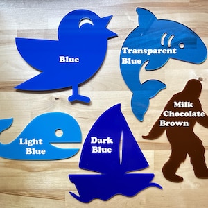 May include: A collection of acrylic cutouts in various shapes and colors. Includes a blue bird, a shark with transparent blue, a whale in light blue, a sailboat in dark blue, and a brown Bigfoot. Each cutout has a color label.